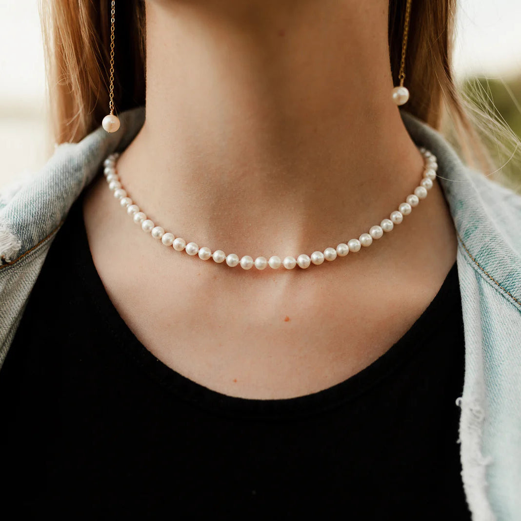Person wearing a pearl necklace with a blurred background