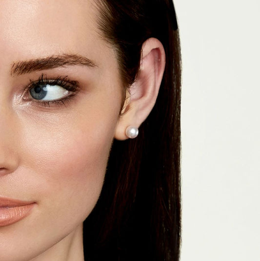 Close-up of a woman's ear wearing a pearl earring with a neutral background