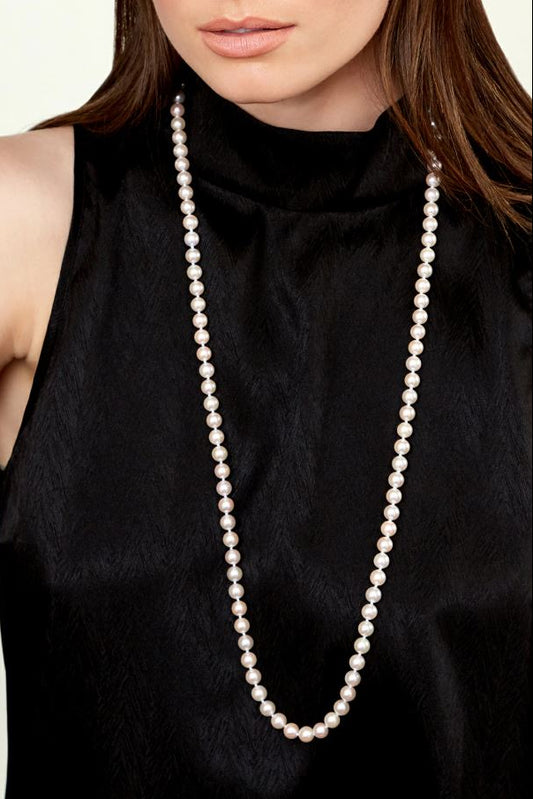Long pearl necklace worn by a person in a black sleeveless top against a neutral background